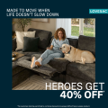 A smiling woman lounges on a dark gray sectional sofa with an extended footrest, petting a golden retriever. Text reads, “Made to move when life doesn’t slow down. Heroes get 40% off.” Loveseat brand logo is in the corner.