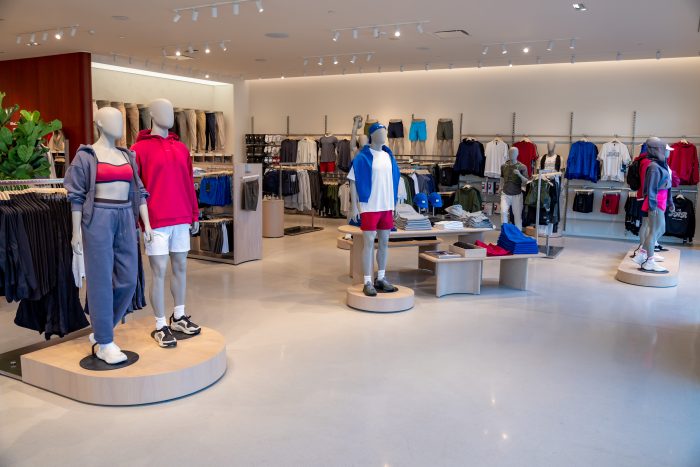 A modern clothing store with mannequins dressed in casual sportswear. Racks of clothes line the walls, and display tables hold neatly folded items. The store is well-lit and spacious.
